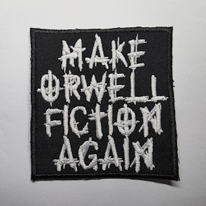 Może przedstawiać: Czarna kwadratowa naszywka z białym haftowanym tekstem. Tekst brzmi "MAKE ORWELL FICTION AGAIN". Naszywka ma szytą obwódkę i lekko zniszczony wygląd. Tekst jest pogrubioną, stylizowaną czcionką.