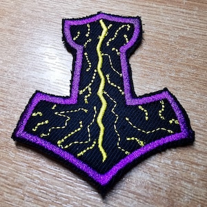 May include: A purple and black embroidered patch with a yellow lightning bolt design. The patch is shaped like a hammer.
