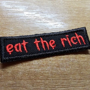 Könnte beinhalten: Schwarzer gestickter Aufnäher mit roter Aufschrift "eat the rich".