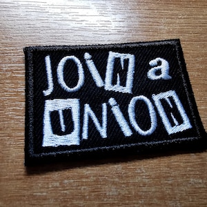 May include: A black fabric patch with white embroidered text that reads "Join a Union".