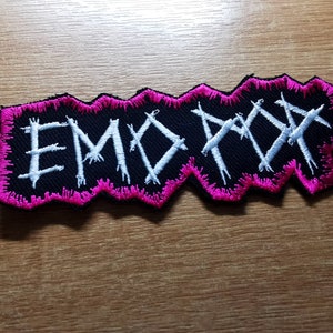 May include: A black and white embroidered patch with the word "EMOPOP" in a jagged font. The patch has a pink border.