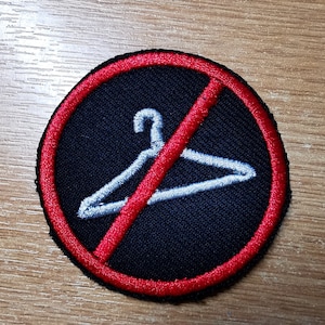 Peut inclure: Un cercle rouge avec une ligne diagonale qui le traverse, interdisant l'utilisation d'un cintre blanc. L'arrière-plan est noir.