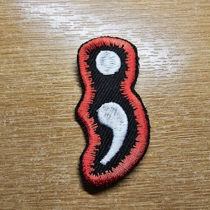 May include: Red and black embroidered patch with a white semicolon symbol.