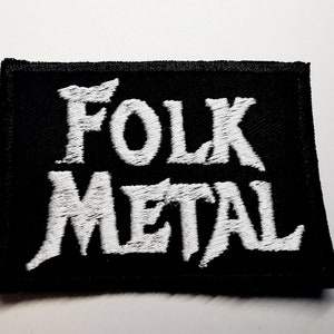 Może przedstawiać: Czarna, prostokątna naszywka z białym, haftowanym napisem „FOLK METAL”. Naszywka jest prawdopodobnie przeznaczona na kurtkę lub torbę i jest wyrazem preferencji muzycznych.