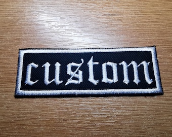 May include: White embroidered "custom" text on a black rectangular patch with a white border.