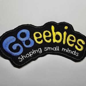 May include: Embroidered patch featuring the words "68 eebies shaping small minds". The patch has a black background with blue and yellow lettering. The patch has an irregular, wavy shape.