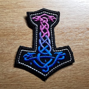 May include: A black embroidered patch of a Viking hammer with a blue and pink braided design.