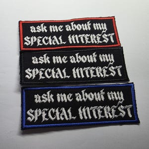May include: Three embroidered patches with the text "ask me about my SPECIAL INTEREST". Each patch is rectangular with a black background and white lettering. The borders are red, black, and blue.