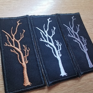 Op de afbeelding: Drie geborduurde patches met een zwarte achtergrond en een wit boomontwerp. De bomen zijn in verschillende kleuren: koper, zilver en paars.