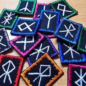 May include: A collection of 15 black fabric patches with white embroidered runes. The patches are surrounded by a colourful border in various colours, including red, blue, green, orange, and pink.