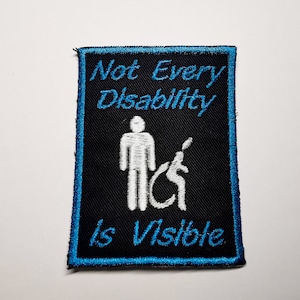 Può includere: Toppa ricamata con sfondo nero e bordo blu. La toppa presenta il testo "Not Every Disability Is Visible" in blu, insieme a un omino stilizzato e un simbolo di sedia a rotelle in bianco.