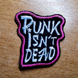 May include: A black embroidered patch with a white outline. The patch says "Punk Isn't Dead" in a stylized font.