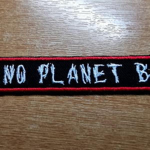 Może przedstawiać: Czarna naszywka haftowana z czerwonym obramowaniem. Naszywka zawiera napis "NO PLANET B" białymi literami.