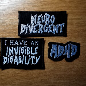 Pode incluir: Tr&ecirc;s patches de tecido preto com texto branco. O patch superior diz "Neuro Divergente". O patch do meio diz "Eu tenho uma defici&ecirc;ncia invis&iacute;vel". O patch inferior diz "TDAH".