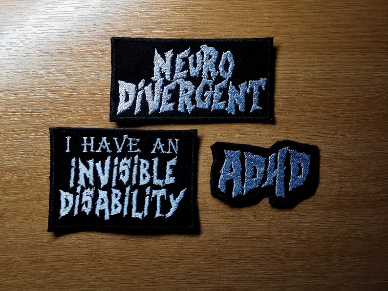 Pode incluir: Tr&ecirc;s patches de tecido preto com texto branco. O patch superior diz "Neuro Divergente". O patch do meio diz "Eu tenho uma defici&ecirc;ncia invis&iacute;vel". O patch inferior diz "TDAH".