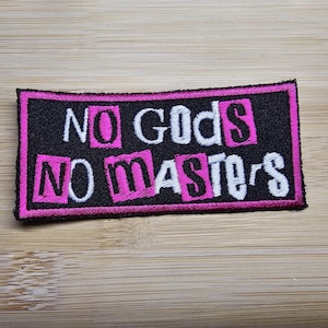 May include: Black patch with pink and white embroidered text that reads "NO GODS NO MASTERS".