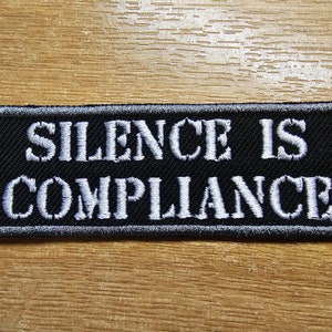May include: Black embroidered patch with white text that reads "Silence is Compliance".