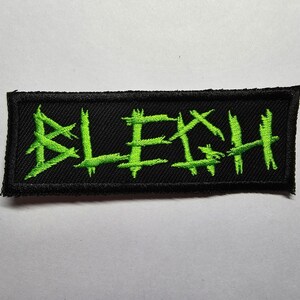 May include: Black patch with green embroidered lettering that reads "BLEGH".