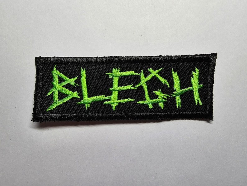 May include: Black patch with green embroidered lettering that reads "BLEGH".