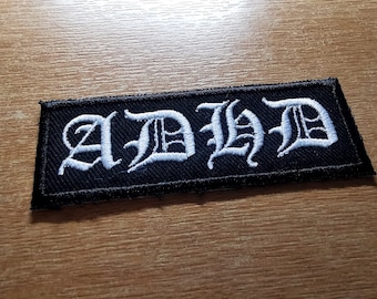May include: Black embroidered patch with white lettering that reads "AD/HD".