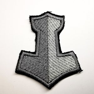 May include: A black and white embroidered patch of a hammer with a pointed top and a rounded bottom.