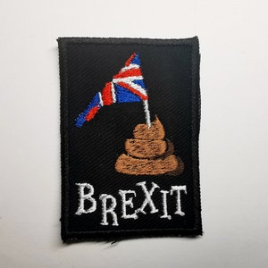 May include: A black embroidered patch with a brown pile of poop topped with a small Union Jack flag. The text "BREXIT" is embroidered in white below the poop.