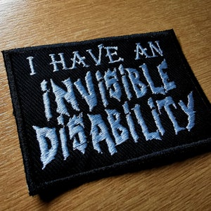 Pode incluir: Patch de tecido preto com texto bordado branco que diz "Eu tenho uma defici&ecirc;ncia invis&iacute;vel".