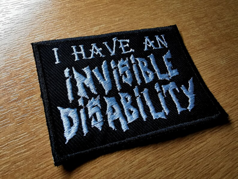 Pode incluir: Patch de tecido preto com texto bordado branco que diz "Eu tenho uma defici&ecirc;ncia invis&iacute;vel".