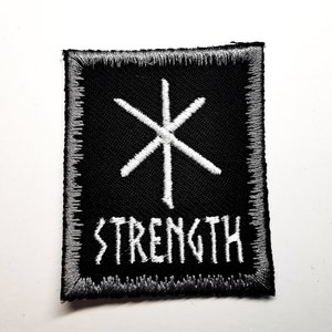 May include: A black and white embroidered patch with a white symbol and the word "STRENGTH" in white lettering.