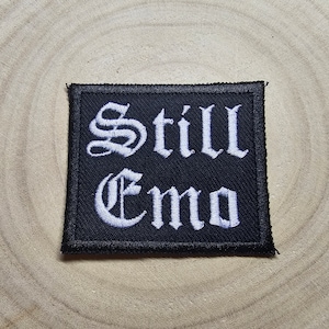 Może przedstawiać: Czarna naszywka haftowana z białym tekstem, który brzmi "Still Emo".