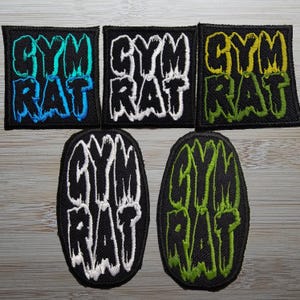 Puede incluir: Seis parches bordados con la inscripción "GYM RAT" en varios colores. Los parches son negros con el texto en azul, blanco, amarillo y verde. Los parches tienen forma cuadrada y ovalada.