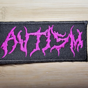 Może przedstawiać: Czarna łatka z tkaniny z wyszytym napisem "ANTHEM" w kolorze różowym.