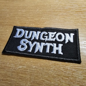 Może przedstawiać: Czarna haftowana naszywka z białym tekstem, który brzmi "Dungeon Synth".