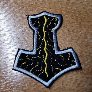 May include: A black embroidered patch with a silver outline depicting a stylized hammer with a yellow lightning bolt design.