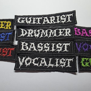 May include: Black embroidered patches with white, yellow, blue, red, purple, and green text. The patches feature the words "Guitarist", "Drummer", "Bassist", "Vocalist", and "Guitar". The text is in a gothic font.