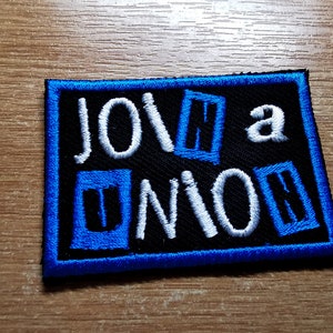 Könnte beinhalten: Blau-weißer gestickter Aufnäher mit dem Text "Join a Union" in weißen Buchstaben auf schwarzem Hintergrund.
