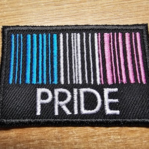 Peut inclure: Un patch brodé noir avec un motif de code-barres en bleu, blanc et rose. Le mot "PRIDE" est brodé en blanc sous le code-barres.