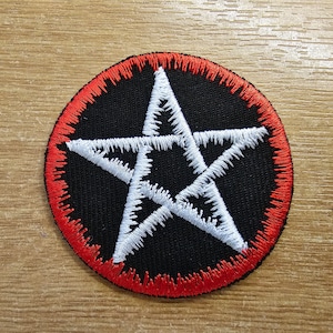 Puede incluir: Un pentagrama blanco bordado sobre un círculo negro con un borde rojo. El parche está hecho de tela y tiene un borde cosido.