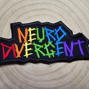 Puede incluir: Un parche de tela negro con las palabras "NEURO DIVERGENT" bordadas en colores arcoíris.