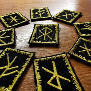 May include: Nine black fabric patches with yellow embroidered runes. The runes are arranged in a circle on a wooden surface.
