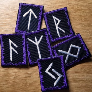 Broderade lappar med vikingarunor, lila kant och vita runor i flerfärgade färger