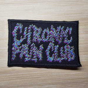 May include: Black embroidered patch with the text "GRAPHIC NOISE" in a colorful, distorted font.