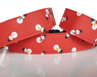 May include: Three red dog collars with a snowman pattern. The collars are made of fabric and have metal buckles.