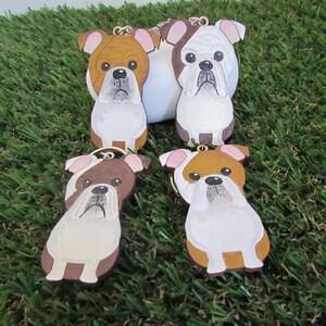 Peut inclure: Quatre porte-clés en bois en forme de bouledogue avec des détails peints. Les bouledogues sont bruns et blancs avec des nez et des yeux noirs. Les porte-clés sont attachés à des anneaux dorés.