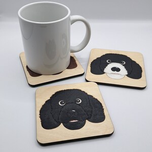 May include: Three wooden coasters featuring black and white illustrations of a dog's face. The coasters are square and have a light wood finish.