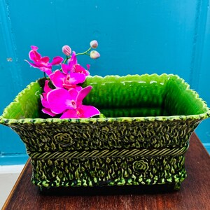 May include: A green ceramic planter with a textured surface and a scalloped rim. The planter is filled with water and has pink orchid flowers in it.