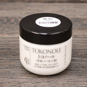 Puede incluir: Un tarro blanco con tapa negra y etiqueta. La etiqueta dice "Tokonole" y "Leather Finish". El tarro contiene un acabado de cuero transparente para proteger y pulir el cuero.