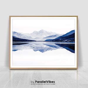Könnte beinhalten: Ein Foto einer Bergkette, die sich in einem stillen See spiegelt. Die Berge sind schneebedeckt und der See ist tiefblau. Der Himmel ist hellblau und in der Ferne sind Wolken zu sehen.
