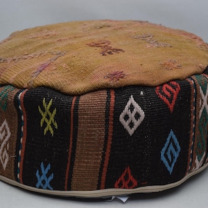 May include: A round, brown and black patterned ottoman with a woven top. The ottoman has a geometric design with red, blue, green, and white accents.