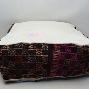 May include: A square, brown and pink patterned cushion with a white, removable cover. The cushion is made of woven fabric and has a geometric design.
